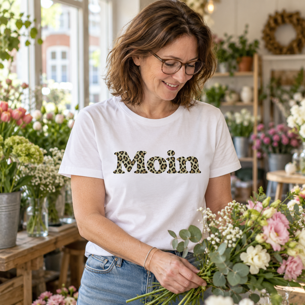 Frau im weißen Bio Unisex T-Shirt mit Moin-Leoprint der Sage-Green-Edition als Frontprint im Blumenladen