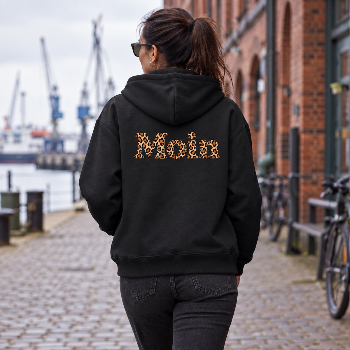 Schwarze Bio Relaxed Zipperjacke von hinten mit Moin-Leoprint in einem norddeutschen Hafenviertel
