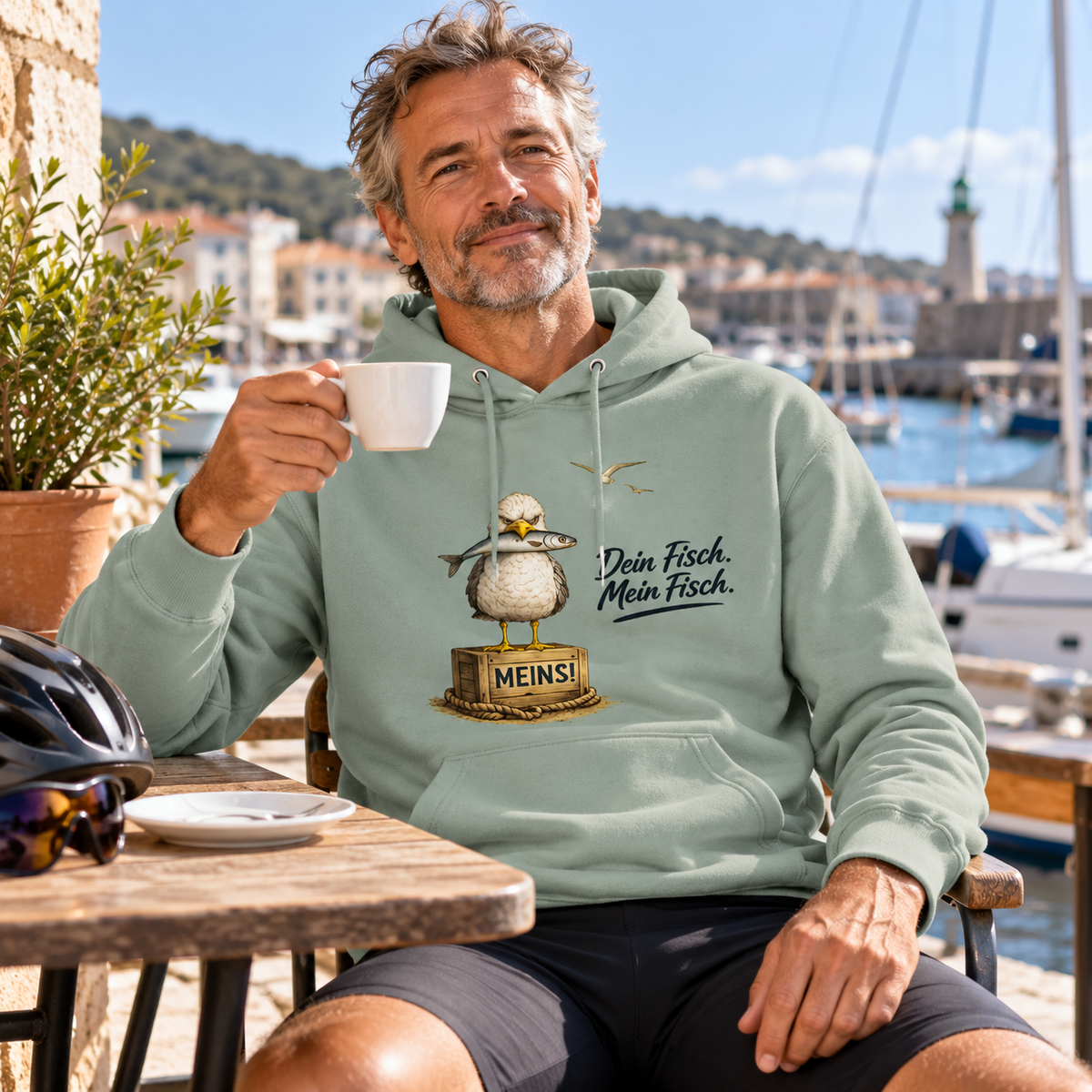 Mann im Bio Hoodie Aloe mit „Dein Fisch. Mein Fisch.“ als Frontprint im Hafencafé