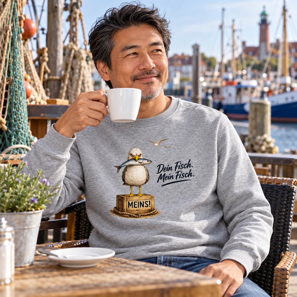 Mann im Bio Unisex Sweatshirt Heather Grey mit Alpha-Möwe und „Dein Fisch. Mein Fisch.“ als Frontprint im Hafencafé