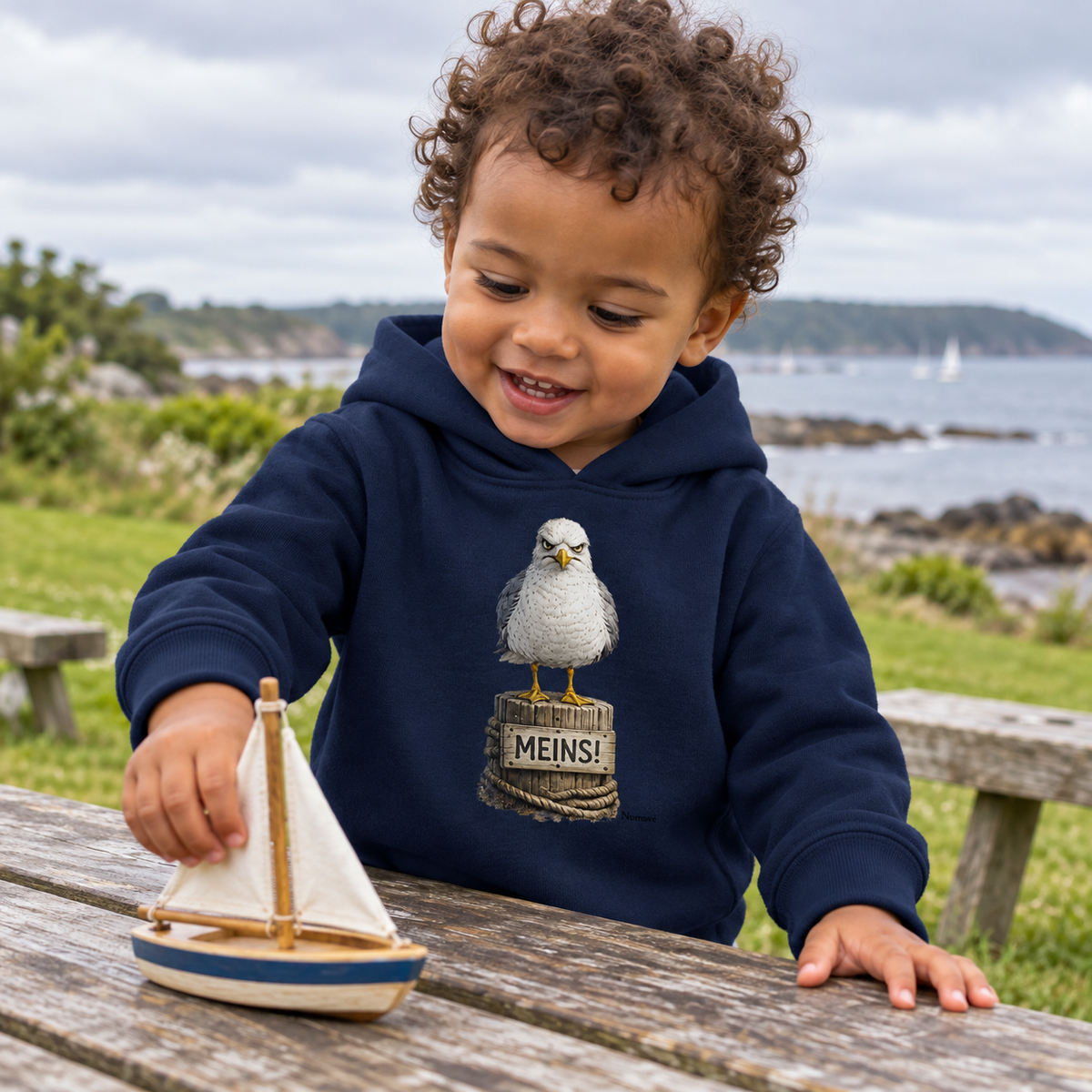 Kleinkind im Baby Bio Hoodie French Navy mit Alpha-Möwe auf Poller und „MEINS!“ als Frontprint im Küstenpark
