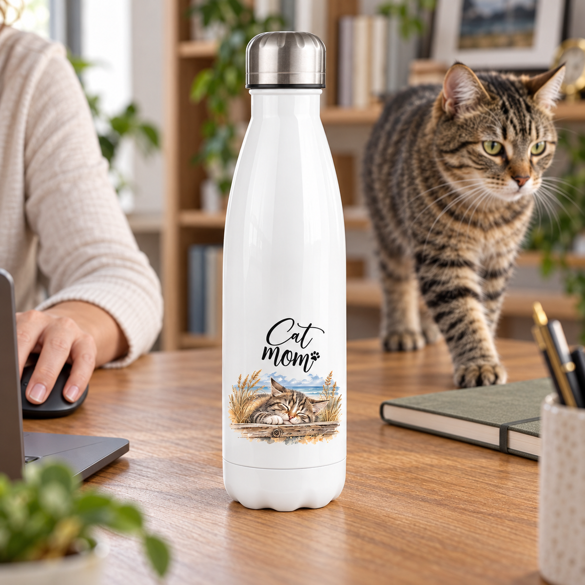 Weiße Cat-Mom-Thermoflasche 500 ml mit silbernem Deckel auf einem Schreibtisch neben einer getigerten Katze.