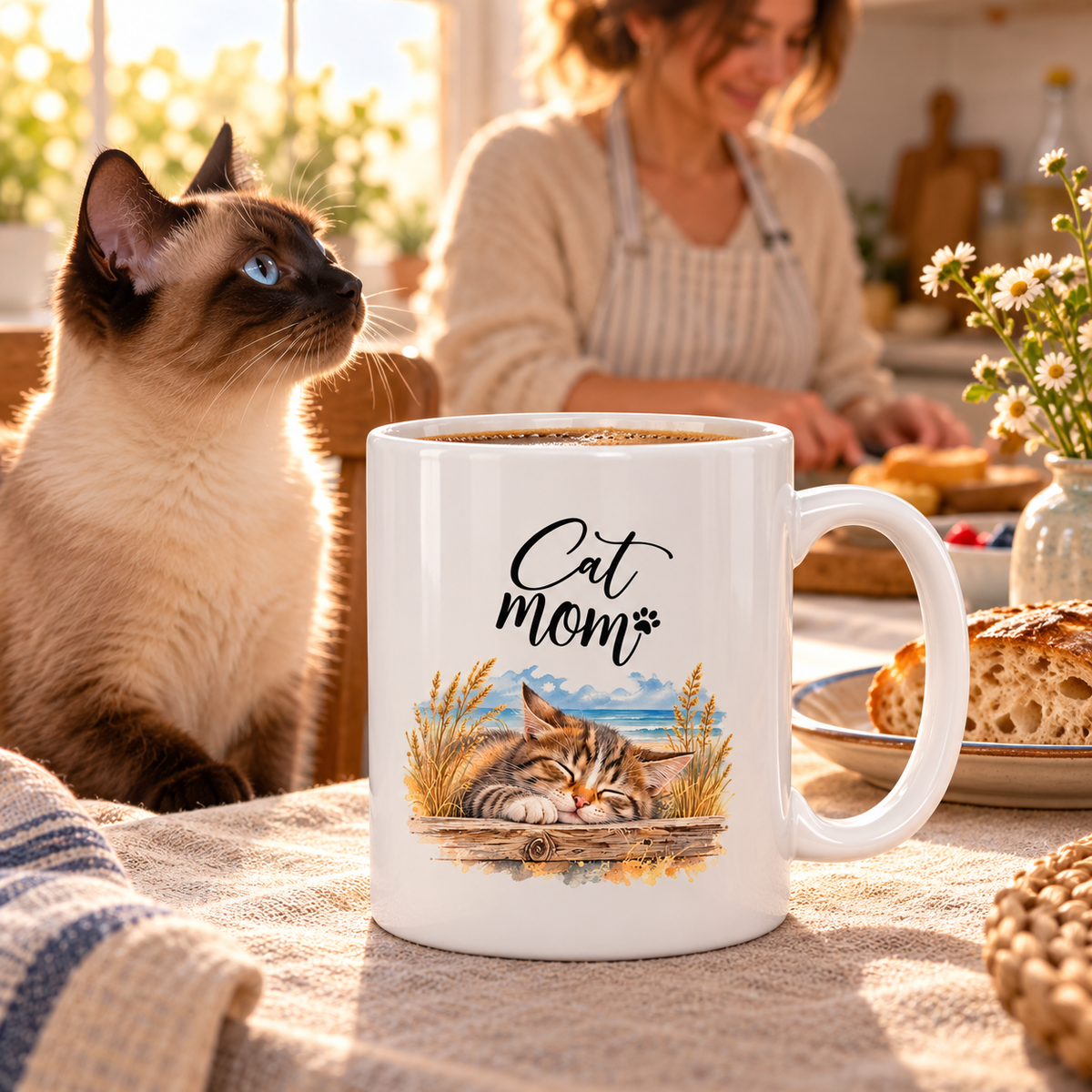 Weiße glänzende Cat-Mom-Tasse mit Katzen- und Küstenmotiv beim Frühstück neben einer Siamkatze.