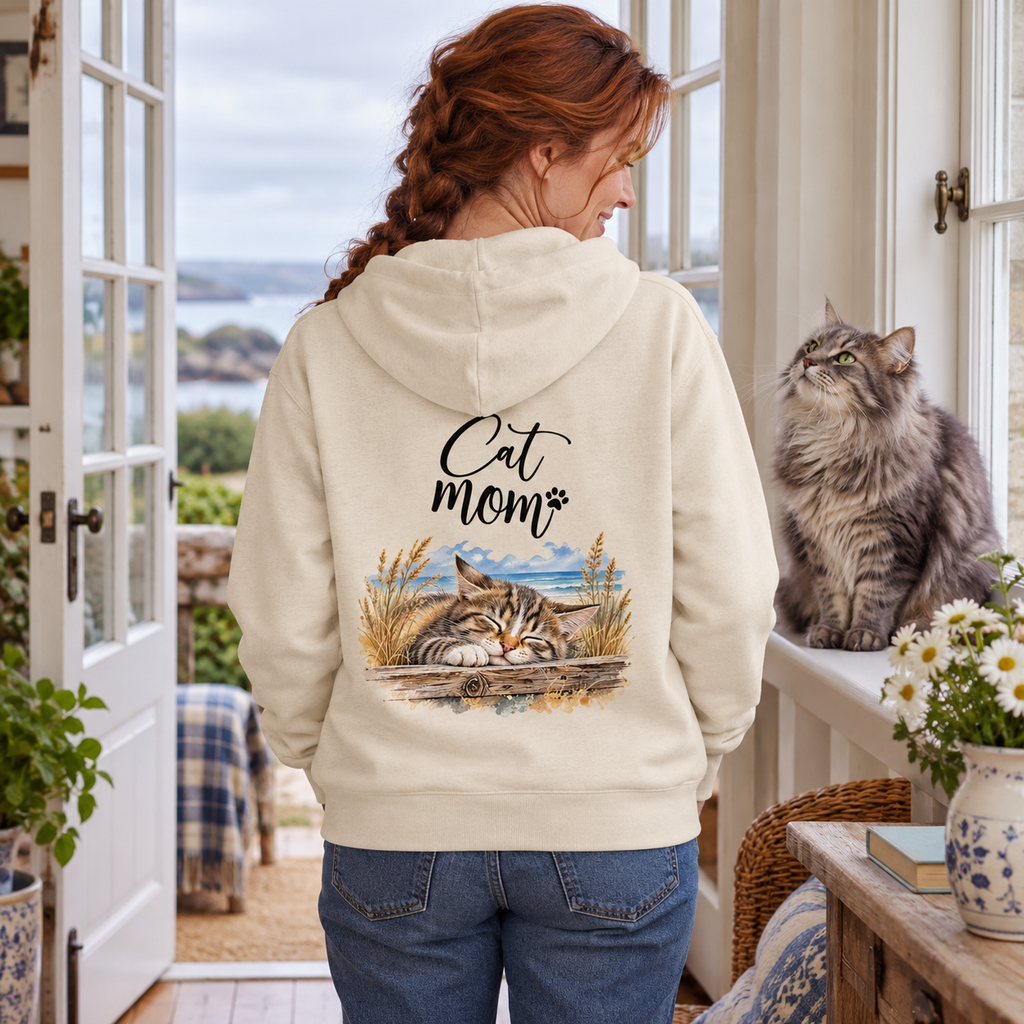 Katzenmama im Bio-Zipper Natural Raw mit Cat-Mom-Backprint neben einer langhaarigen Katze am Fenster.