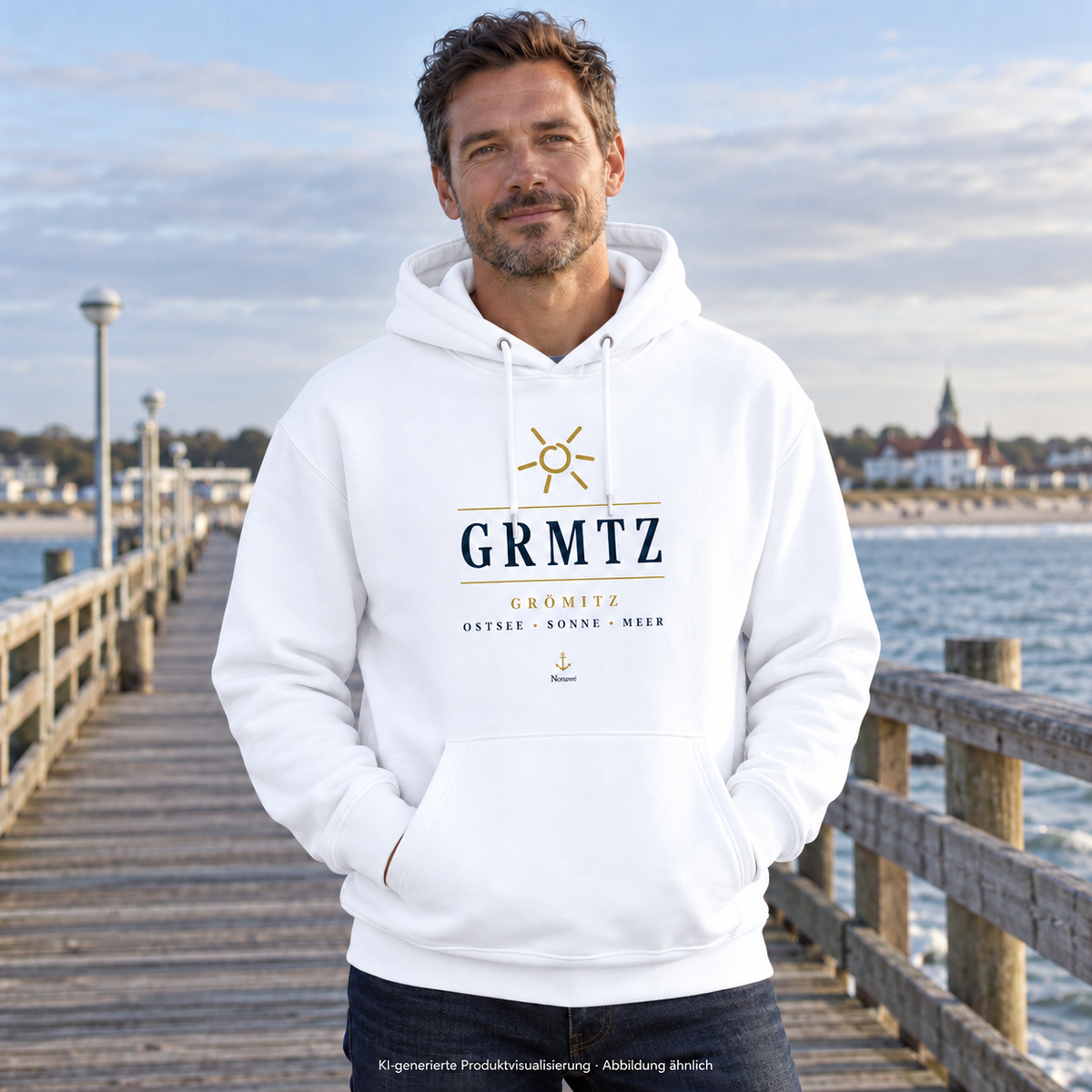 Mann trägt den weißen GRMTZ Grömitz Bio-Hoodie auf einem Steg am Meer – Frontdruck mit Sonne und Anker; KI-Visualisierung.
