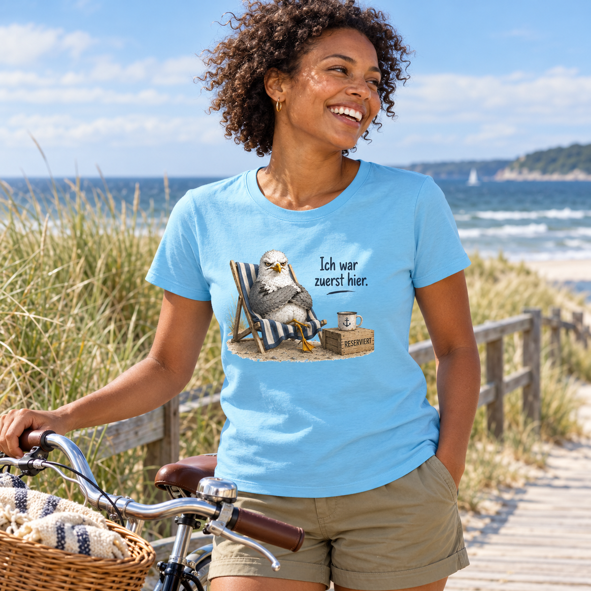 Frau im aqua-blauen Damen Bio T-Shirt mit Möwen-Frontprint und Fahrrad an der Küste
