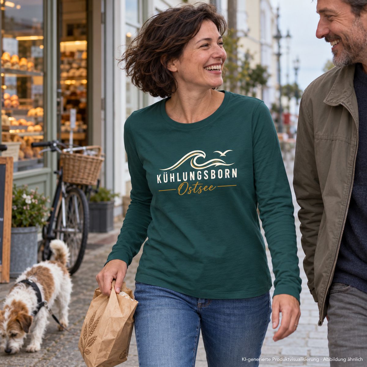 Kühlungsborn Baltic Waves – Bio-Unisex-Longsleeve, Dark Edition, Glazed Green – beim Lachen mit Partner vor einer Bäckerei, Frontdruck; KI-generierte Produktvisualisierung.