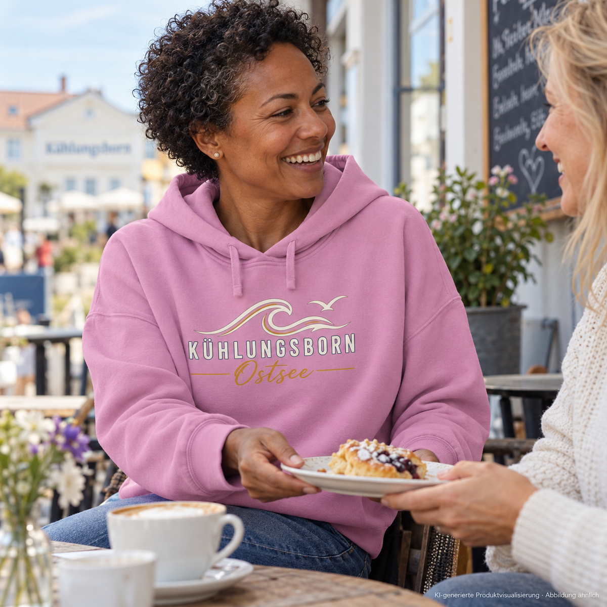 Kühlungsborn Baltic Waves – Damen Bio-Boxcut-Hoodie, Dark Edition, Bubble Pink – beim gemeinsamen Cafébesuch, Frontdruck; KI-generierte Produktvisualisierung.