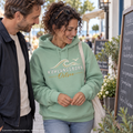 Kühlungsborn Baltic Waves – Bio-Oversize-Hoodie, Dark Edition, Misty Jade – beim gemeinsamen Blick auf eine Cafékarte, Frontdruck; KI-generierte Produktvisualisierung.