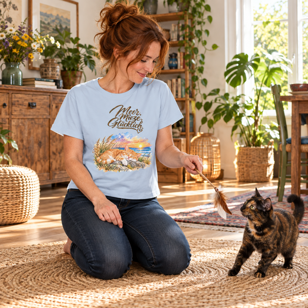 Frau im Damen-Bio-T-Shirt in Blue Soul mit Meer. Mieze. Glücklich.-Frontmotiv spielt auf einem Teppich mit einer Schildpattkatze.