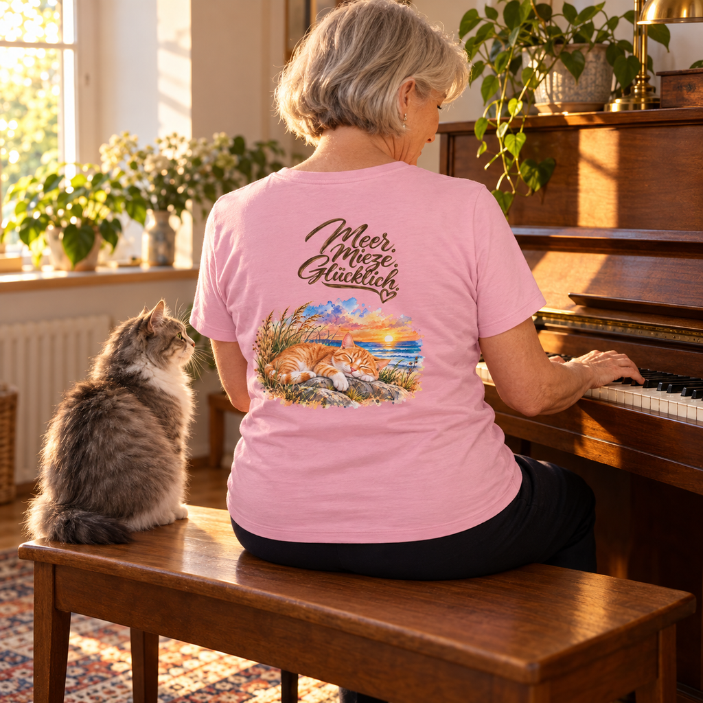 Frau im Damen Bio-T-Shirt in Cotton Pink mit Katzen-Backprint sitzt am Klavier neben einer langhaarigen grau-weißen Katze.