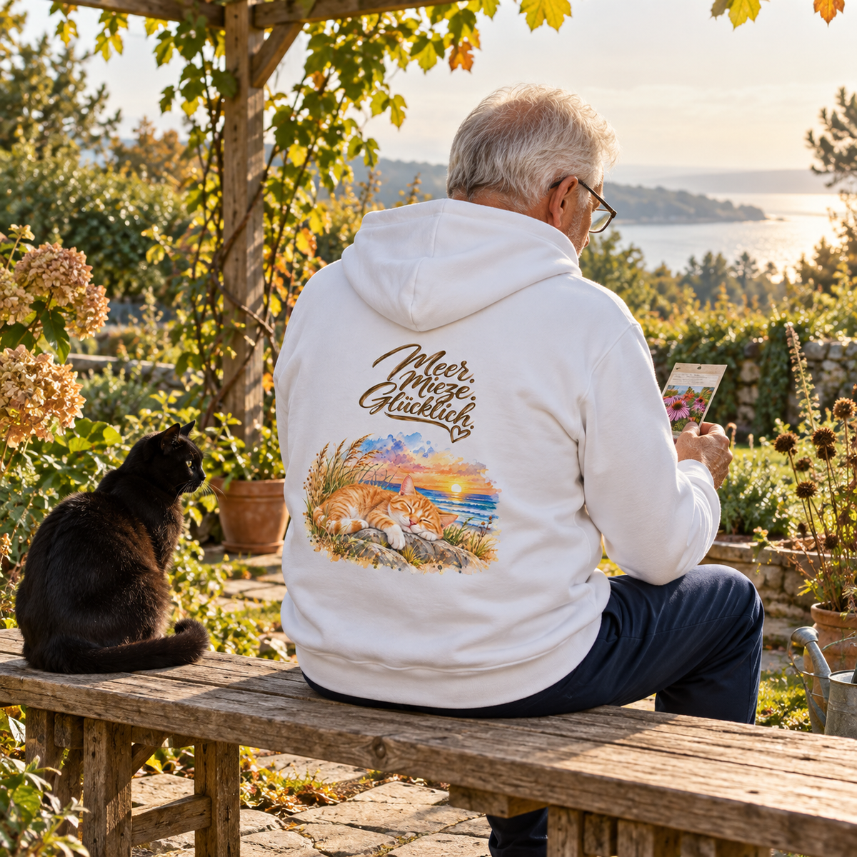 Mann im weißen Bio-Hoodie mit „Meer. Mieze. Glücklich.“ als Backprint sitzt auf einer Gartenbank neben einer schwarzen Katze.