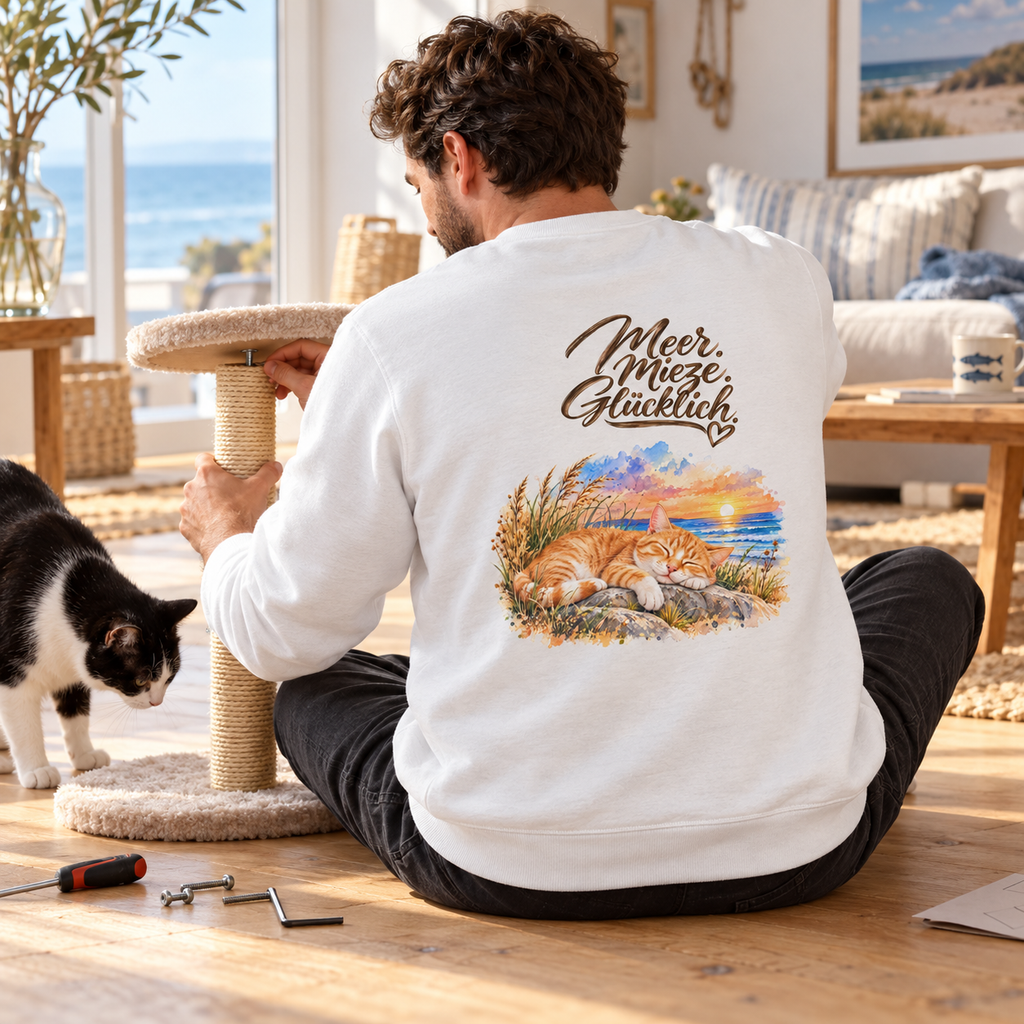Mann im weißen Unisex-Sweatshirt mit „Meer. Mieze. Glücklich.“-Backprint beim Aufbau eines Kratzbaums, neben ihm eine schwarz-weiße Katze.