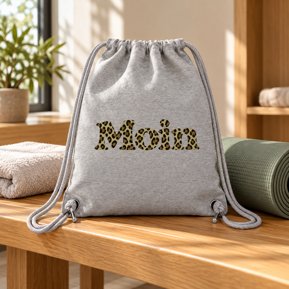 Gym-Bag in Heather Grey mit Moin-Leoprint in Sage Green auf einer Bank neben Yogamatte und Handtuch.