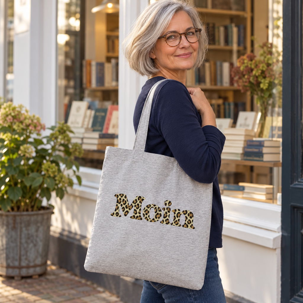 Frau trägt den graumelierten Moin-Leo-Sage-Green-Shopper vor einer Buchhandlung.