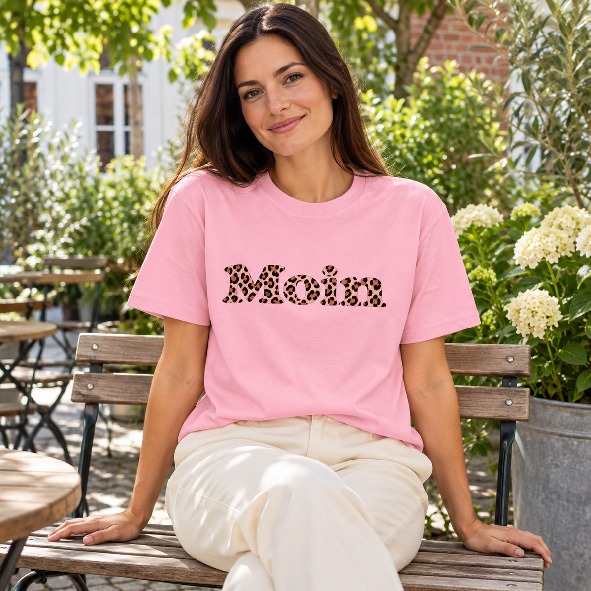 Frau im Gartencafé mit Bio-Unisex-T-Shirt in Cotton Pink und Moin-Leo-Blush-Pink-Motiv.