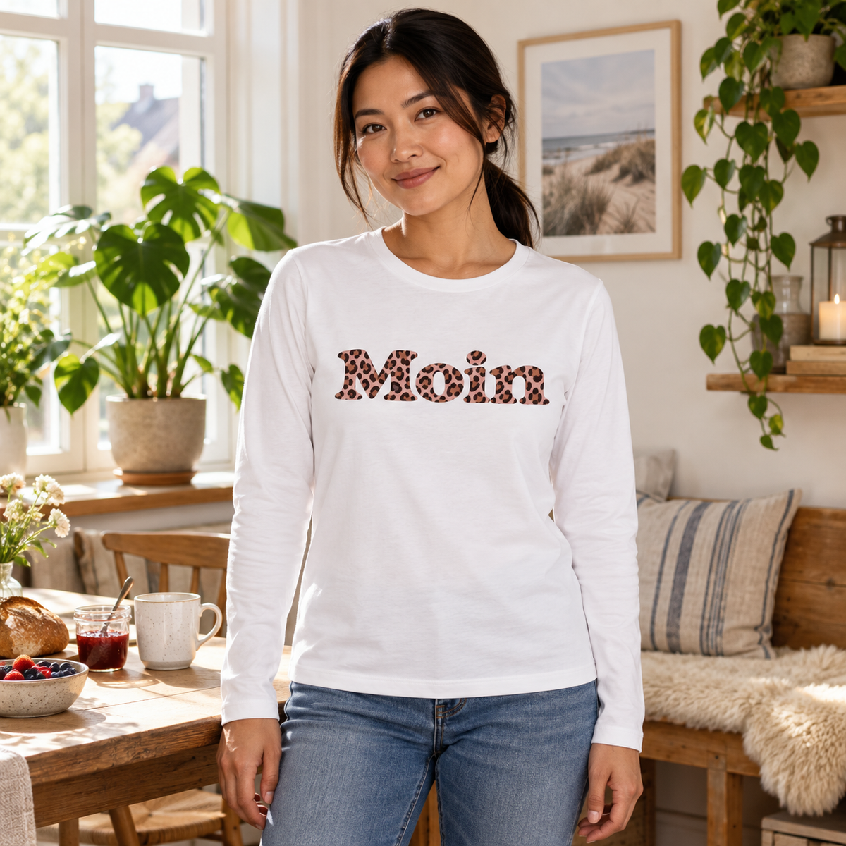 Frau zu Hause trägt ein weißes Damen-Bio-Longsleeve mit Moin-Leo-Blush-Pink-Motiv.