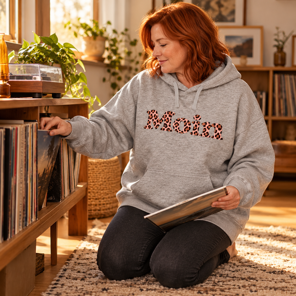 Frau wählt Schallplatten im Bio-Oversize-Hoodie in Heather Grey mit Moin-Leo-Blush-Pink-Motiv.