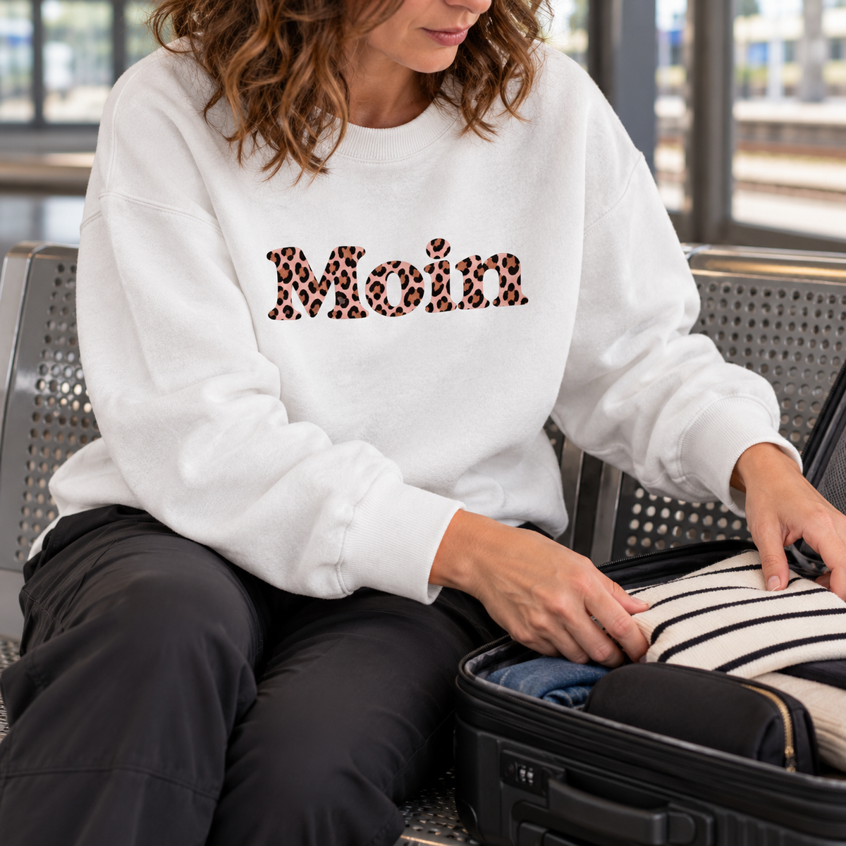 Frau packt Reisegepäck im weißen Bio-Oversize-Sweatshirt mit Moin Leo Blush Pink auf der Vorderseite.