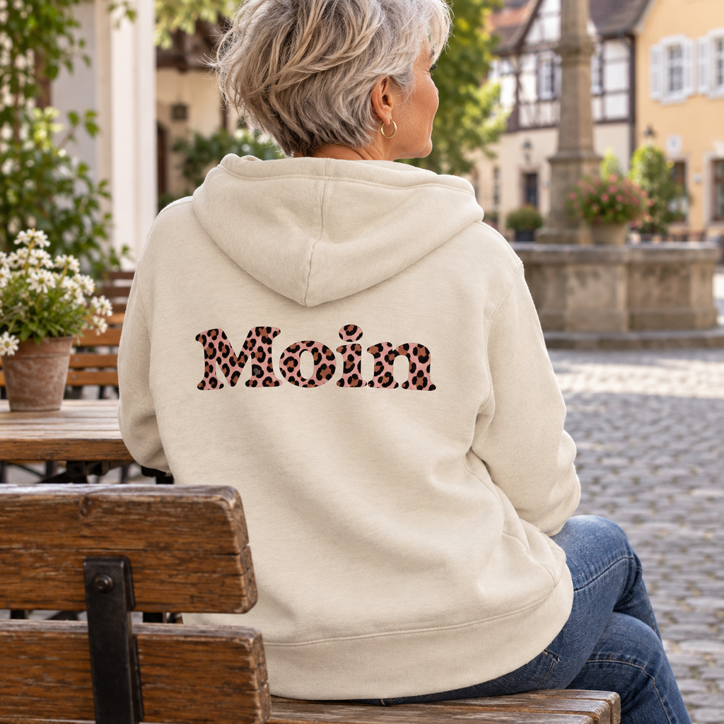 Frau sitzt im Café in der Bio-Zipper-Kapuzenjacke Natural Raw, Rückenansicht mit Moin Leo Blush Pink.