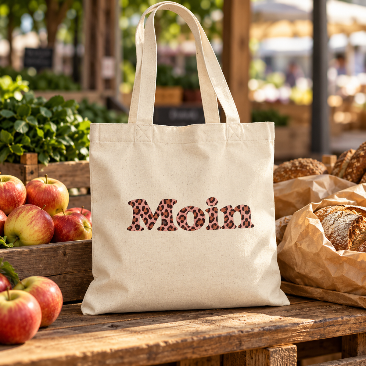 Tote-Bag Natural mit Moin Leo Blush Pink neben Äpfeln und Brot auf einem Marktstand.