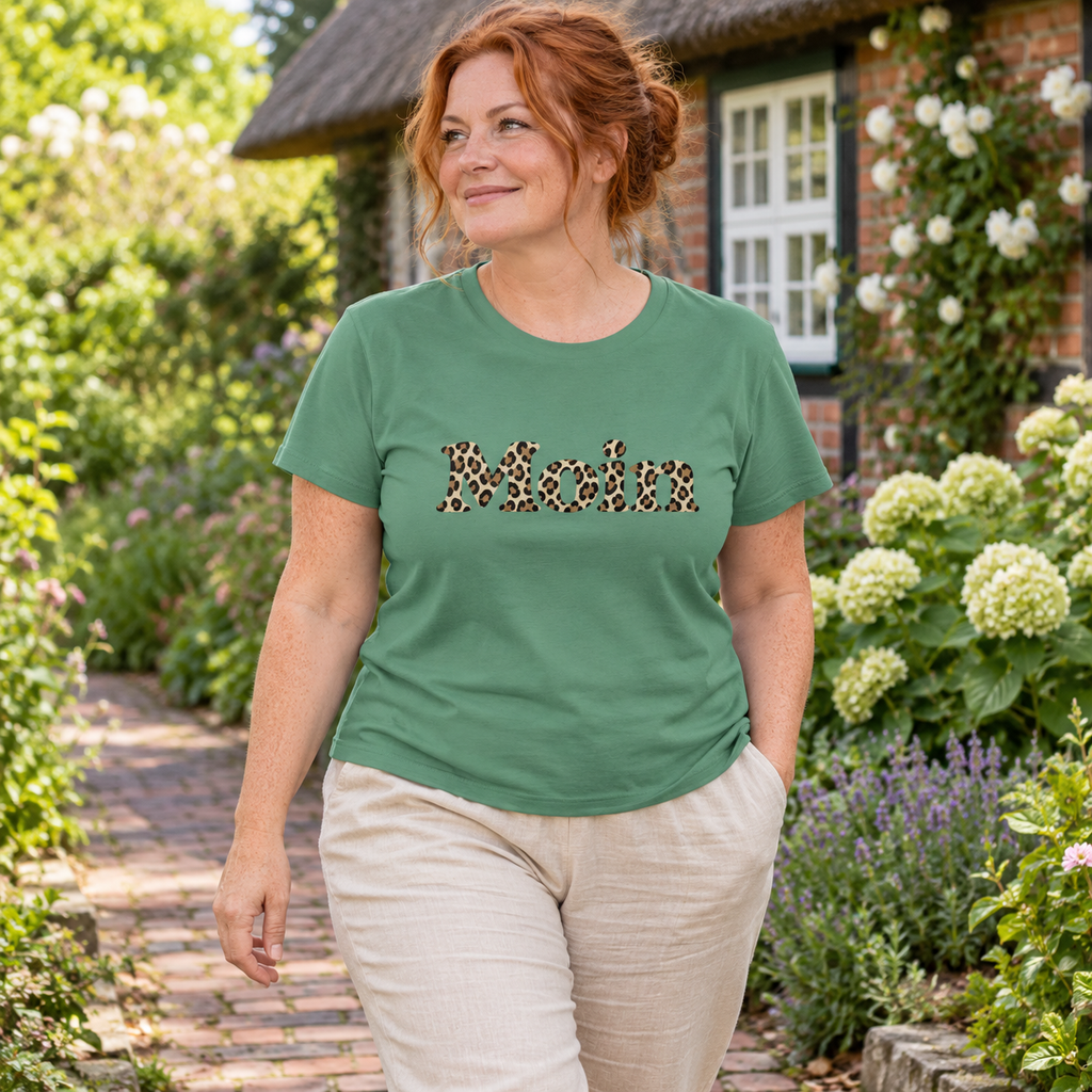 Frau im Damen Bio T-Shirt in Green Bay mit Moin-Leoprint in Sage Green auf einem Gartenweg, Vorderansicht.