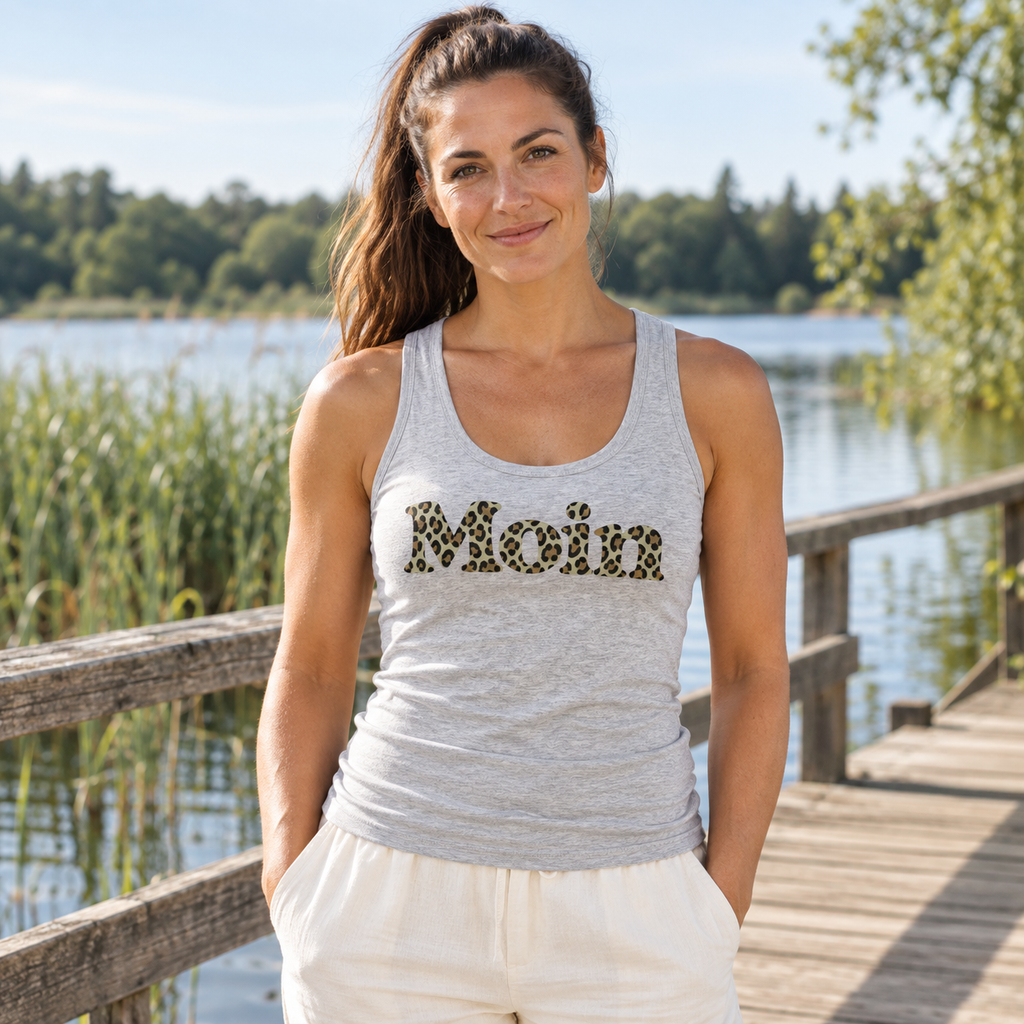 Frau im Damen Bio Fitted Tank Top in Cool Heather Grey mit Moin-Leoprint in Sage Green an einem See, Vorderansicht.