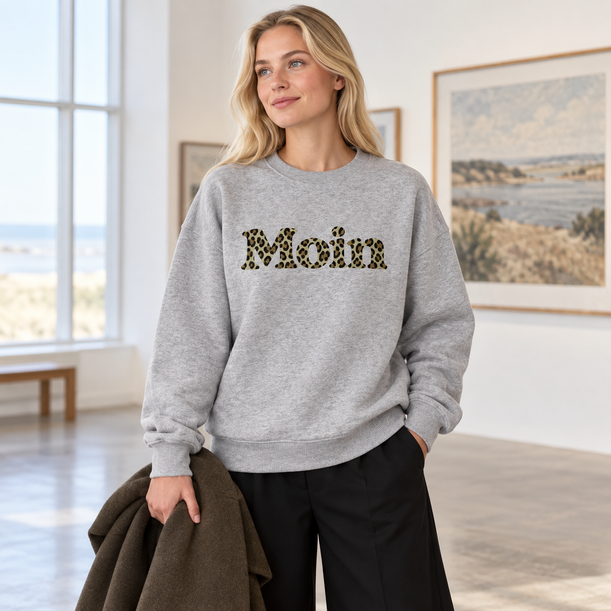 Frau im Bio Oversize Sweatshirt in Heather Grey mit Moin-Leoprint in Sage Green in einer Galerie, Vorderansicht.