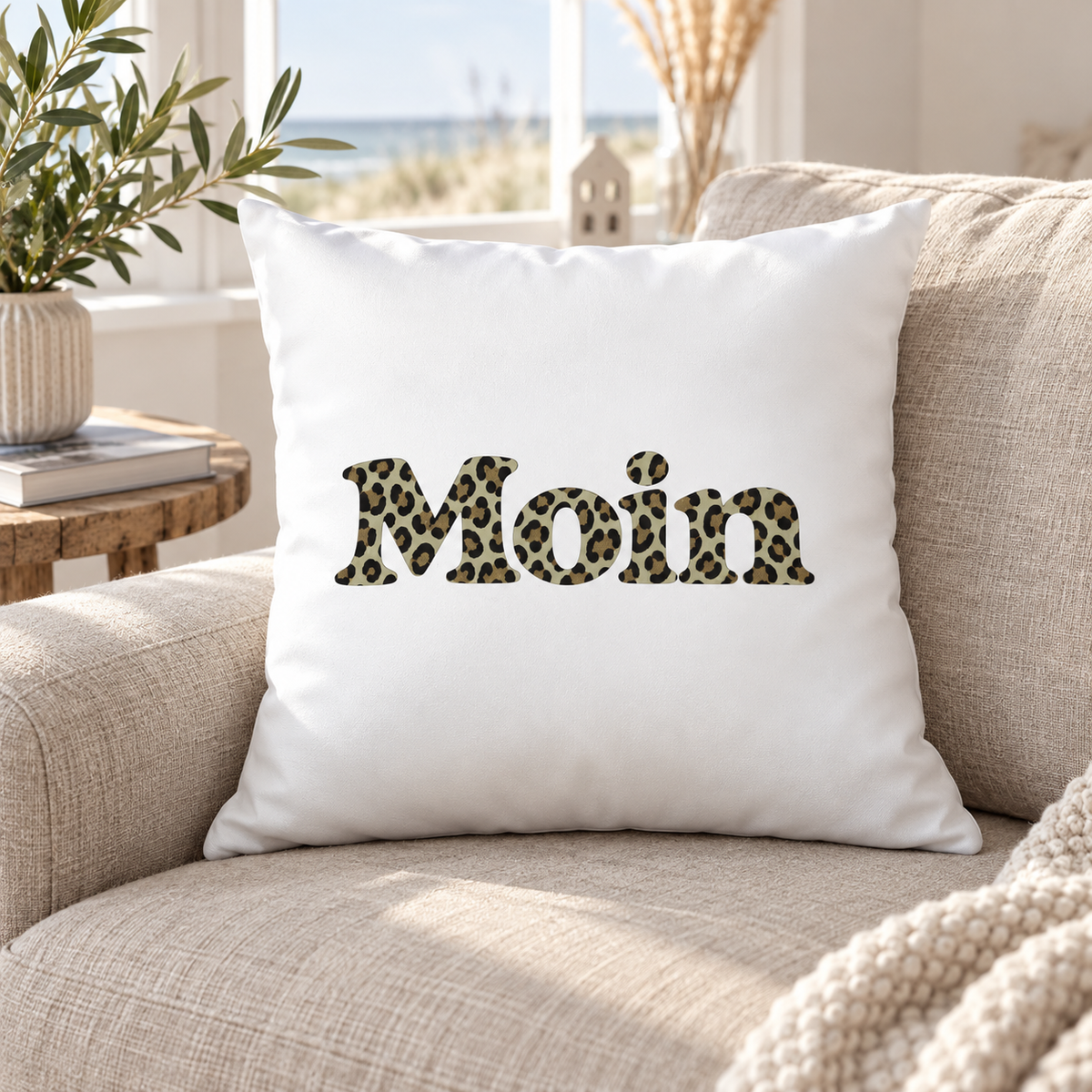 Weißes Kissen 40 × 40 cm mit Moin-Leoprint in Sage Green auf einem beigen Sofa, Vorderansicht.