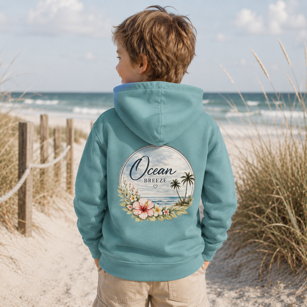 Kind am Strand mit türkisfarbenem Ocean Breeze Kinder Hoodie und floralem Meeresmotiv als Rückendruck