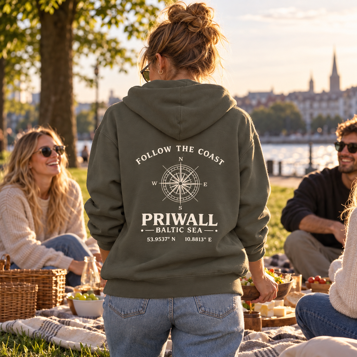 Frau im khakifarbenen Priwall Follow the Coast Bio Hoodie mit Rückenmotiv beim Parkpicknick