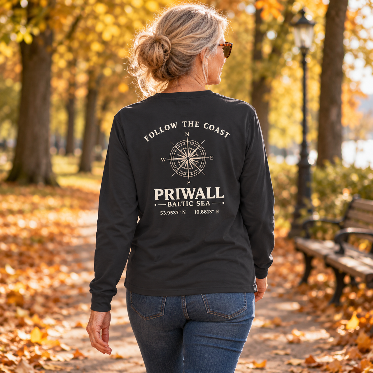 Ältere Frau im schwarzen Priwall Follow the Coast Bio Longsleeve mit Rückenmotiv bei einem Herbstspaziergang
