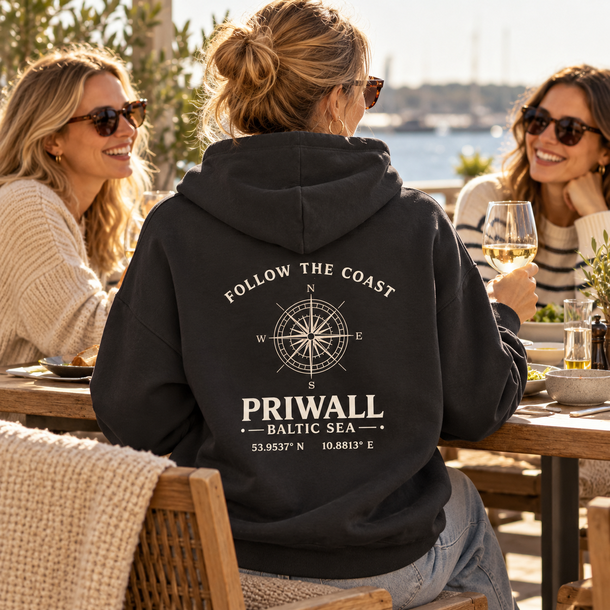 Frau im schwarzen Priwall Follow the Coast Bio Oversize Hoodie mit Backprint auf einer Restaurantterrasse