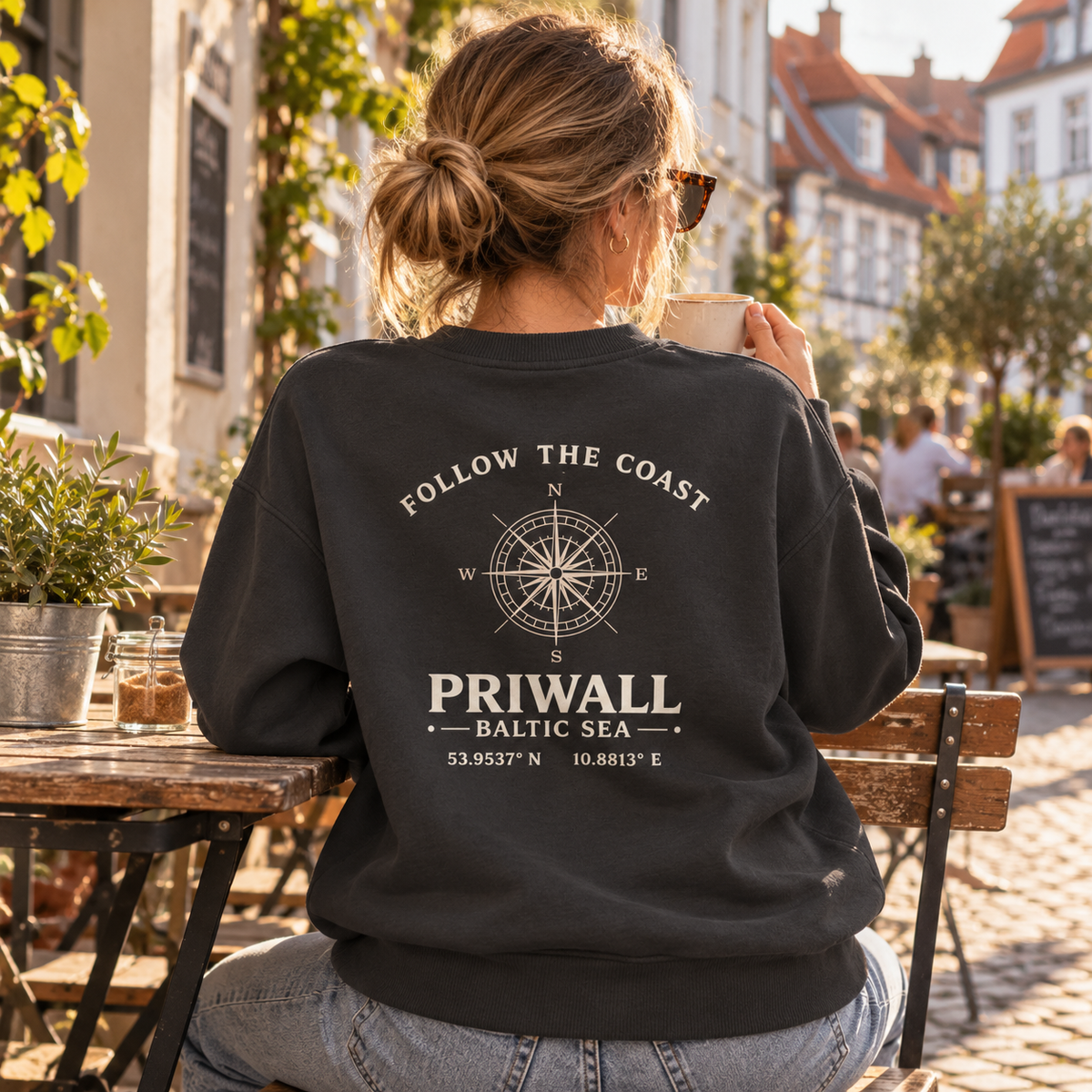 Frau im dunklen Priwall Follow the Coast Bio Oversize Sweatshirt mit Backprint im Straßencafé