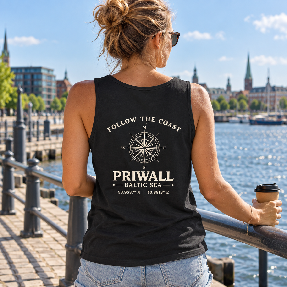 Frau im schwarzen Priwall Follow the Coast Bio Tank Top mit Rückenmotiv an der Uferpromenade