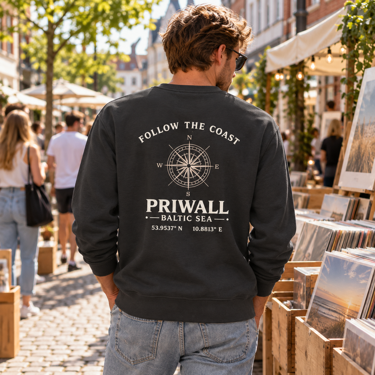 Mann im schwarzen Priwall Follow the Coast Bio Unisex Sweatshirt mit Backprint auf einem Stadtmarkt