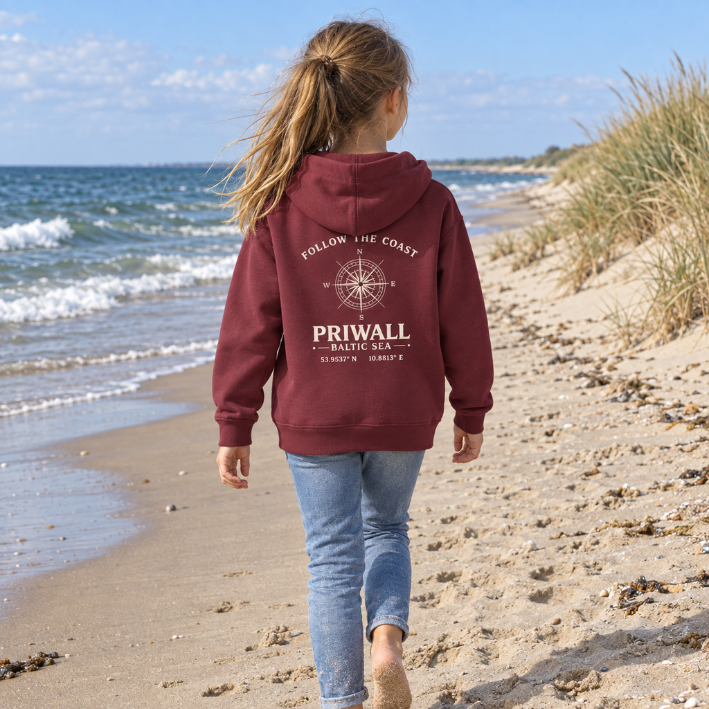 Mädchen trägt burgundyfarbenen Priwall Follow the Coast Kinder-Bio-Hoodie mit Rückenprint am Ostseestrand