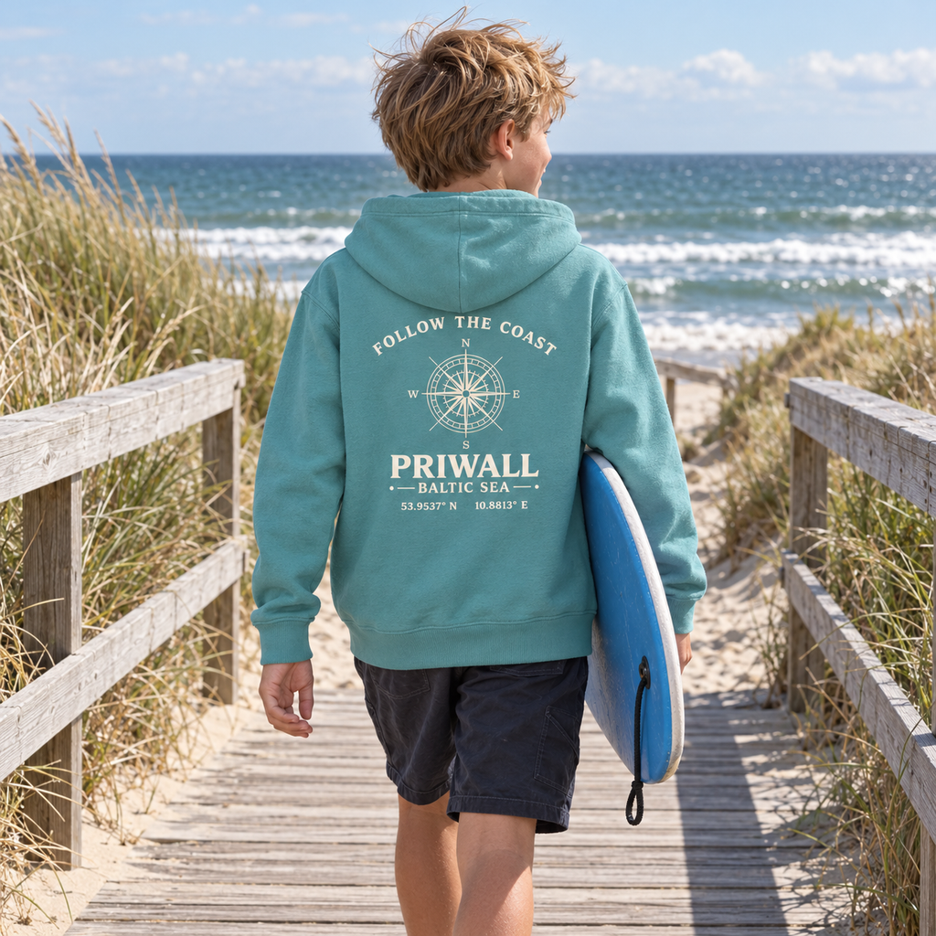Junge trägt hellblauen Priwall Follow the Coast Kinder-Bio-Hoodie mit Rückenprint am Dünenweg