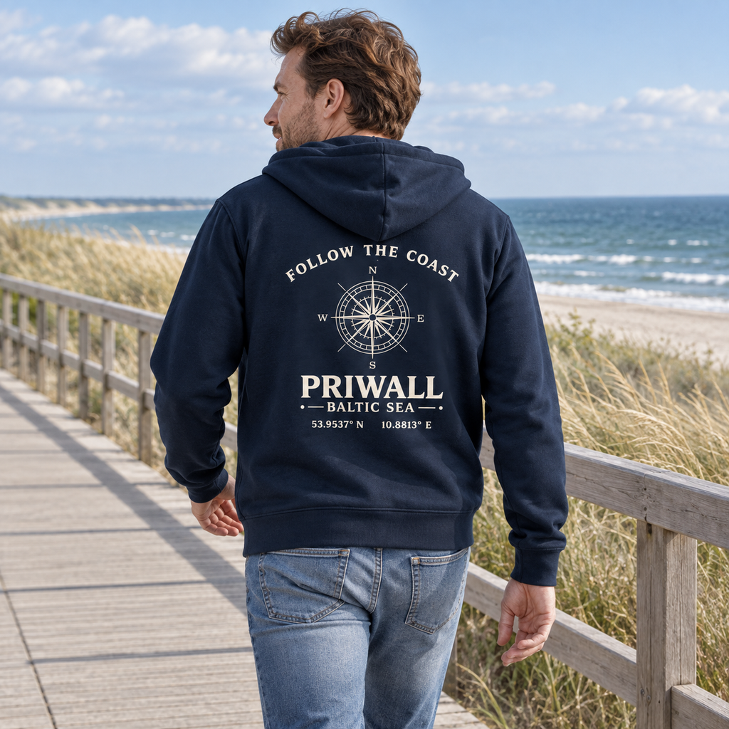 Mann trägt dunkelblaue Priwall Follow the Coast Bio-Kapuzenjacke mit Rückenprint an der Ostsee