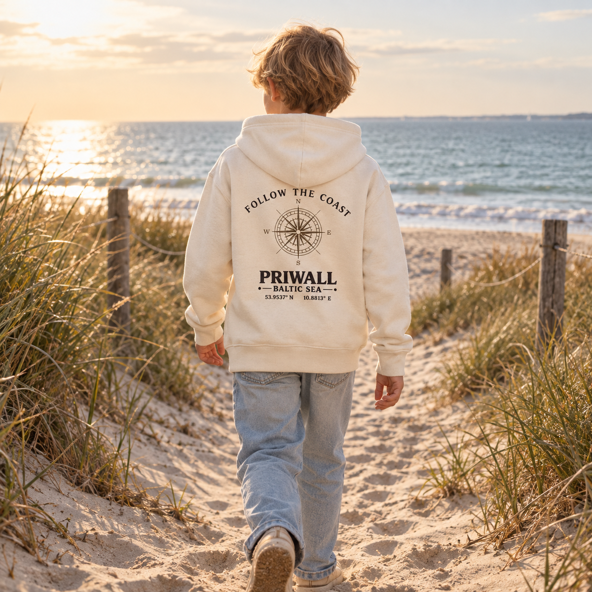 Kind trägt den Priwall Follow the Coast Kinder Bio-Hoodie in Natural Raw auf einem Dünenweg an der Ostsee