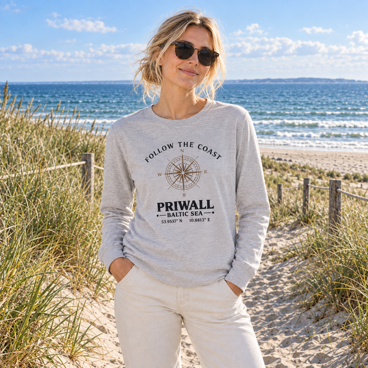 Frau trägt das graue Follow the Coast Priwall Unisex Bio-Longsleeve am Ostseestrand