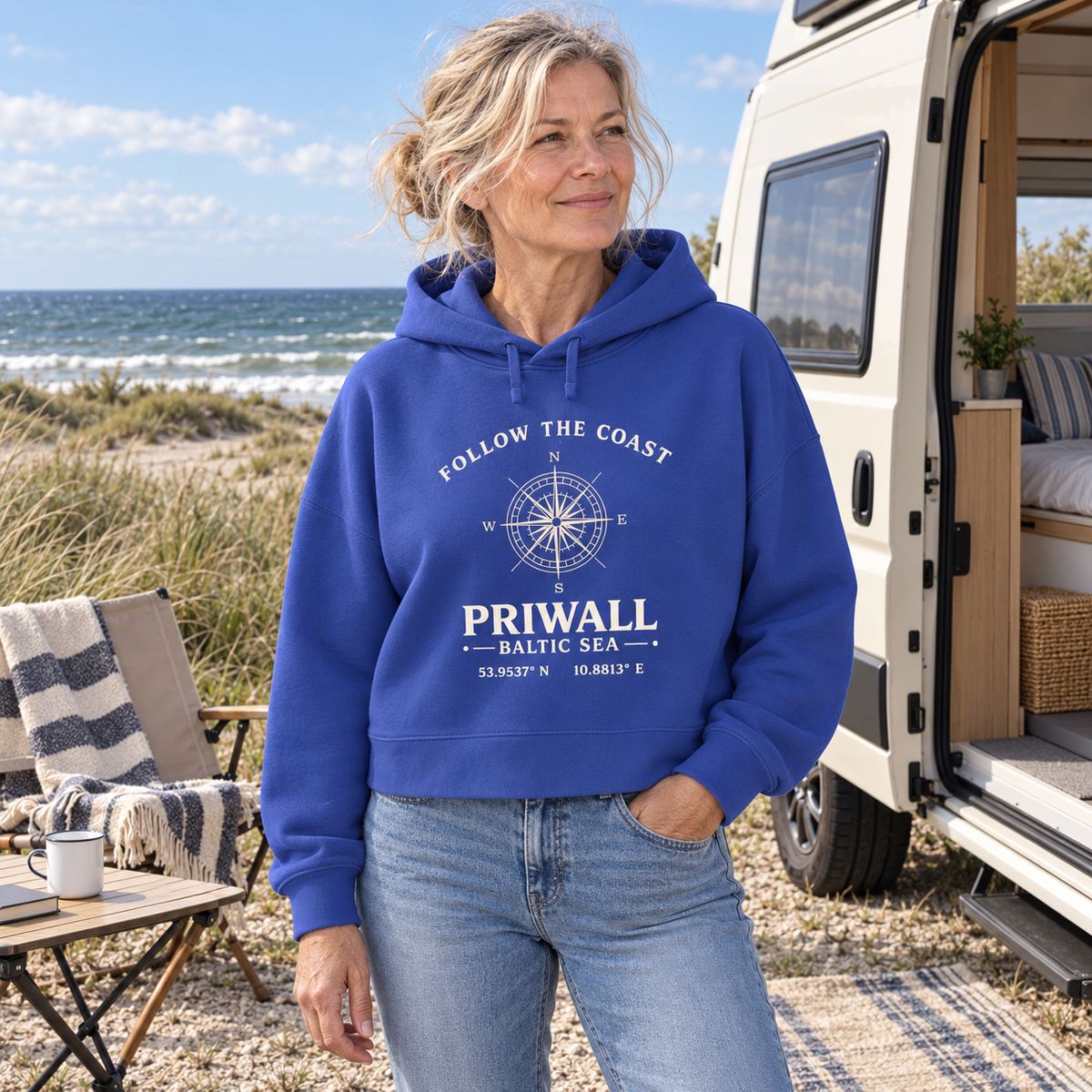 Frau trägt Priwall Kompass Dark Edition Damen Boxcut Hoodie in Worker Blue am Ostsee-Campingplatz