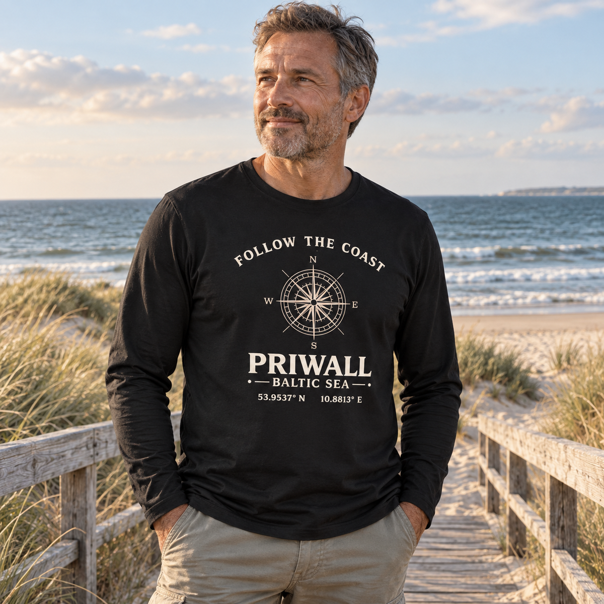 Mann trägt Priwall Kompass Dark Edition Organic Longsleeve in Schwarz am Ostseestrand