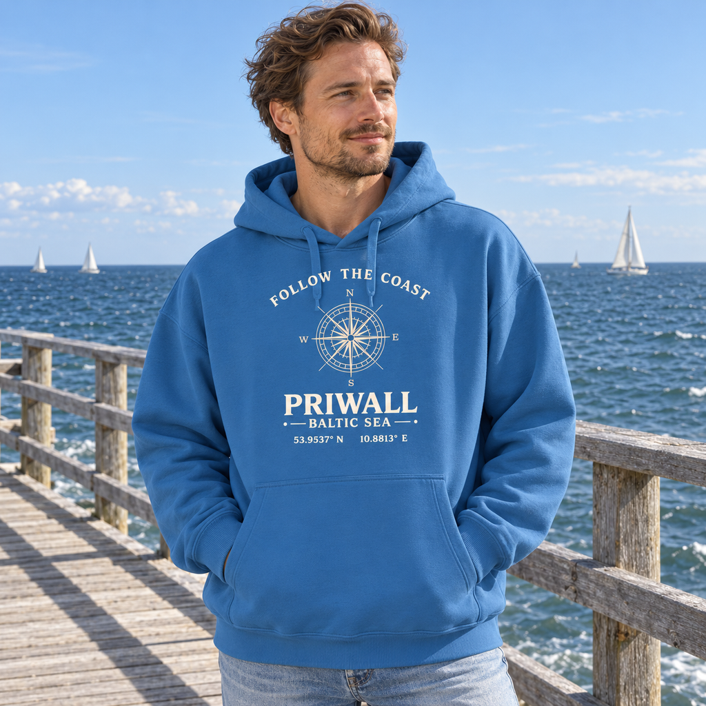 Mann trägt Priwall Kompass Dark Edition Organic Oversize Hoodie in Mindful Blue auf einer Ostsee-Seebrücke