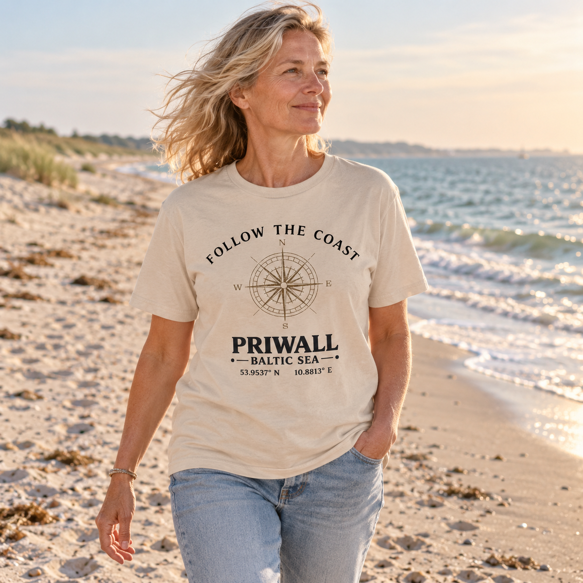 Frau trägt Follow the Coast Priwall Kompass Essential T-Shirt am Ostseestrand