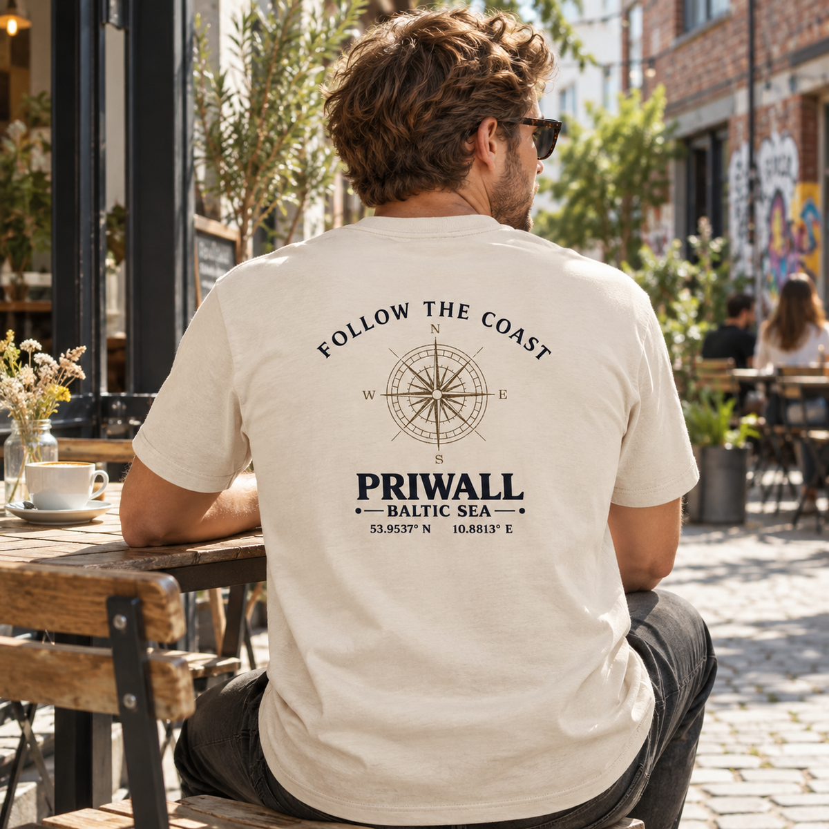 Mann im Bio Heavy T-Shirt mit hellem Priwall Backprint an einem Stadtcafé