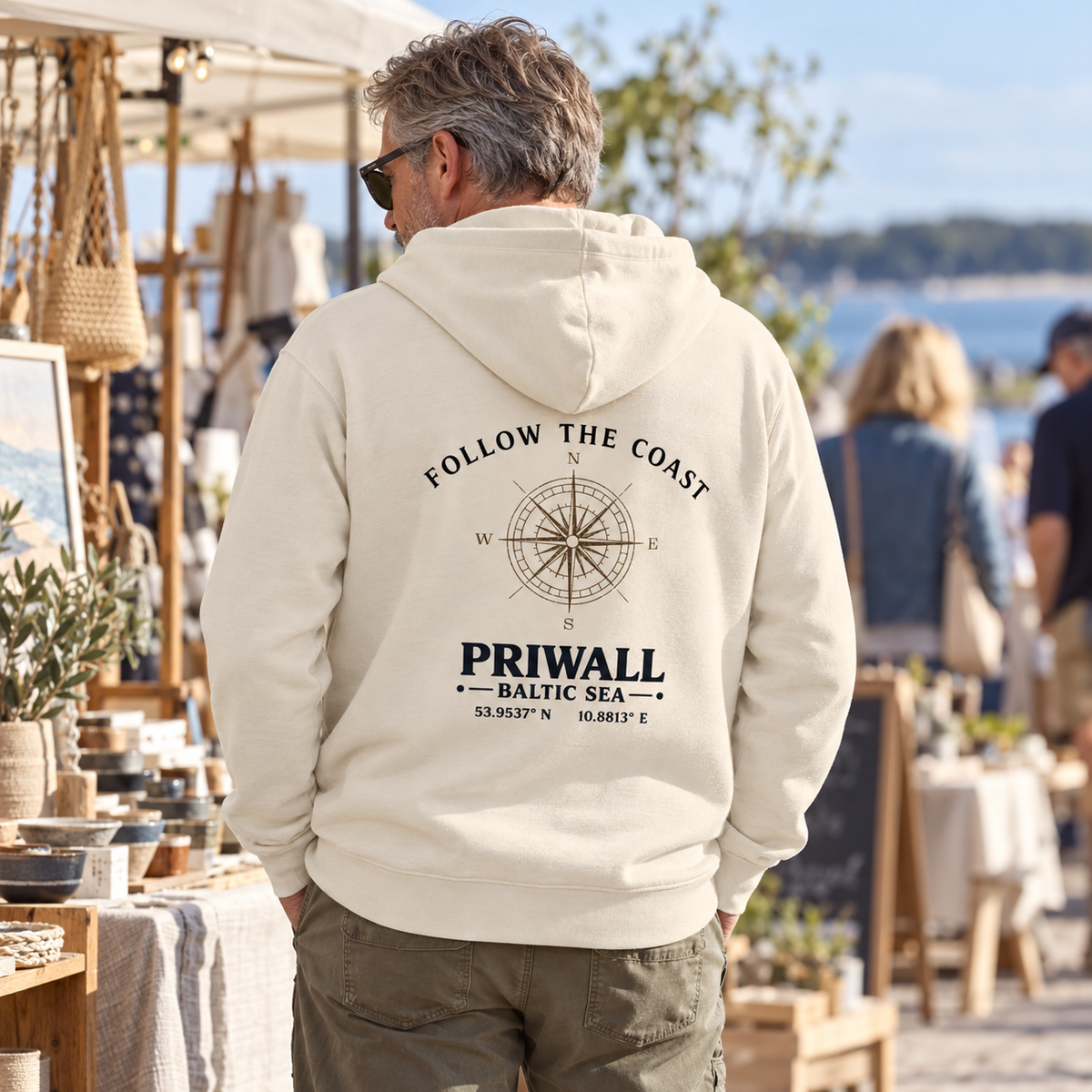 Mann im Bio Hoodie mit hellem Priwall Follow the Coast Backprint auf einem Designmarkt