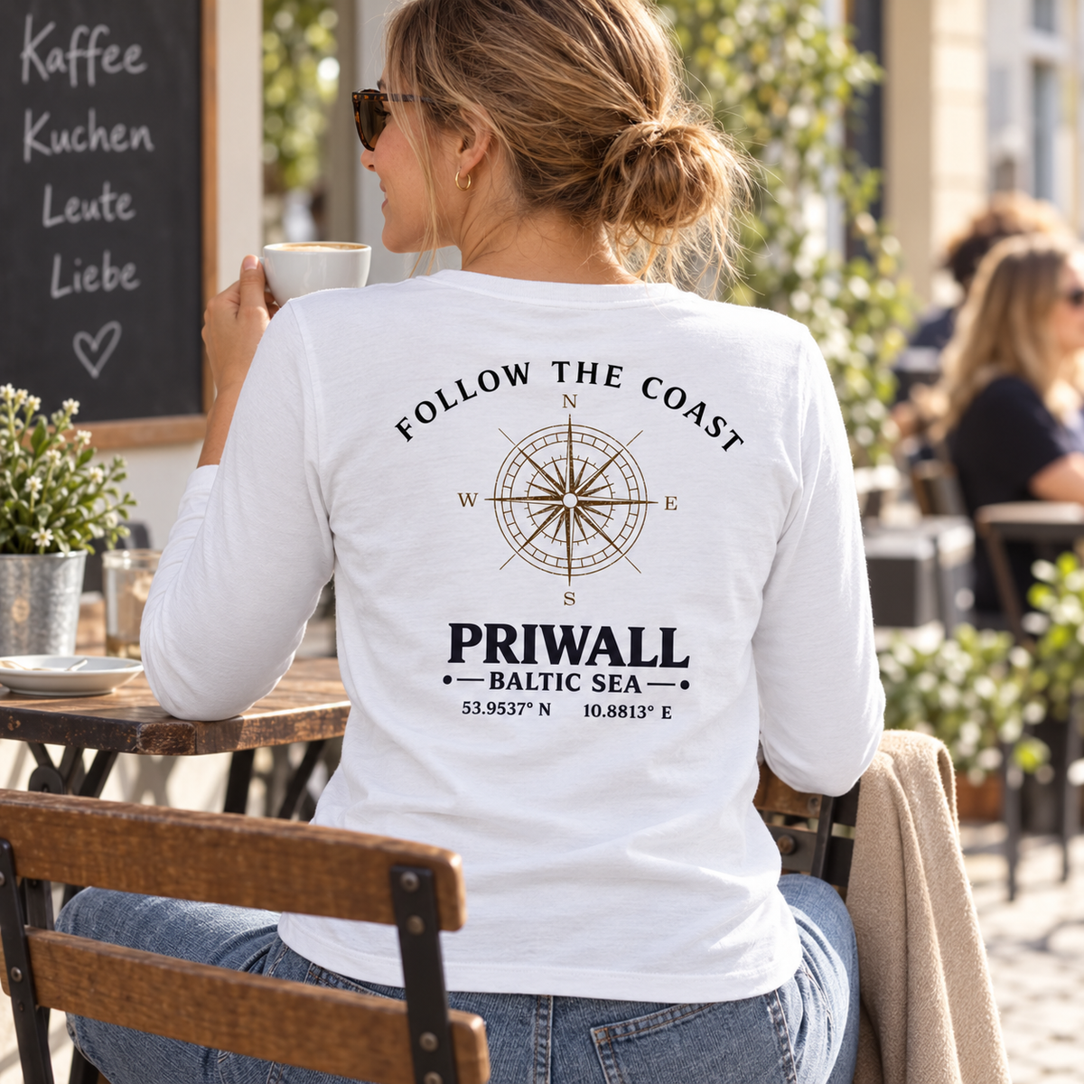 Frau im Damen Bio Longsleeve mit hellem Priwall Follow the Coast Backprint an einem Straßencafé