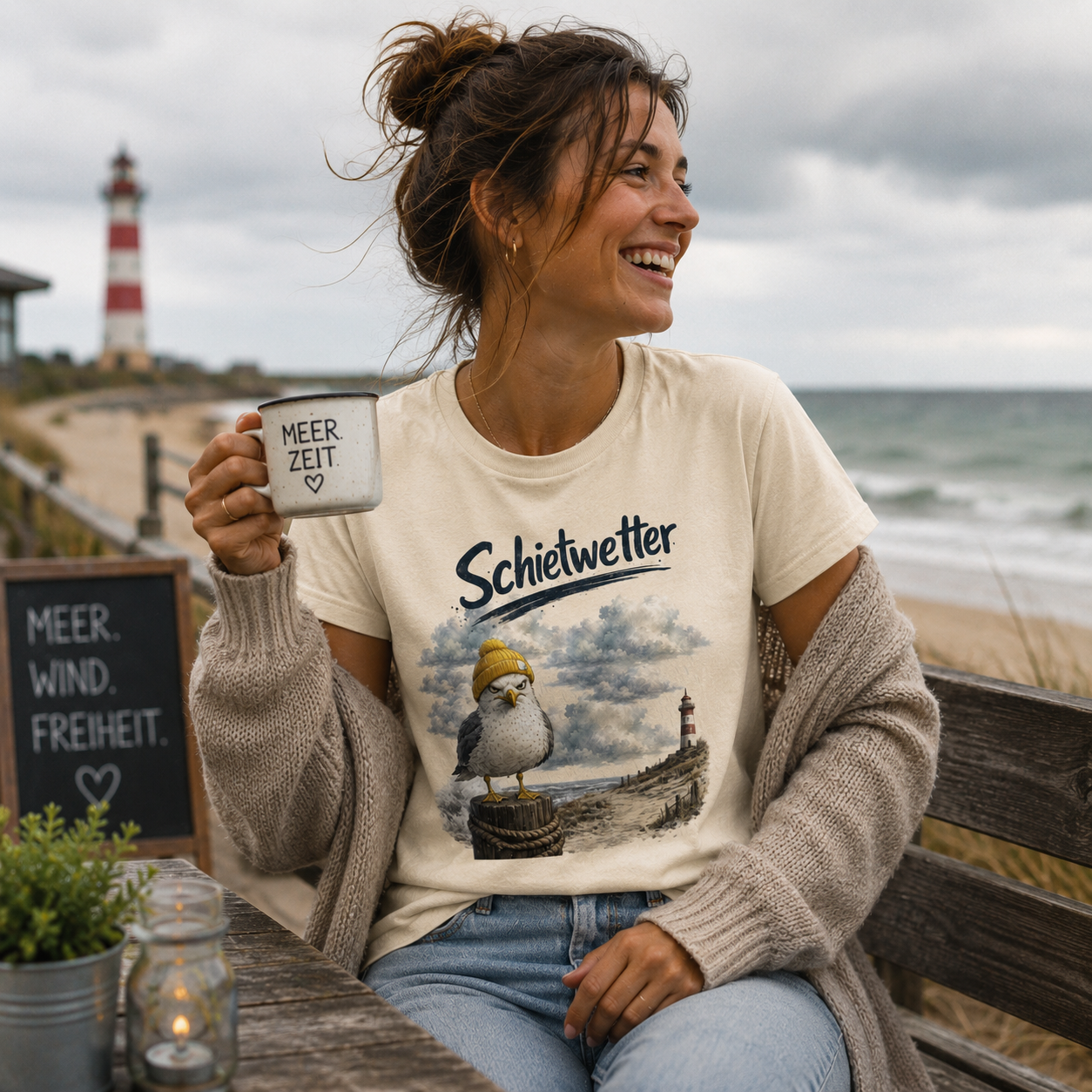 Frau trägt das Nomavé Bio T-Shirt „Schietwetter“ mit frecher Möwe und gelber Mütze, sitzt mit einer Tasse Kaffee am Ostseestrand bei Schietwetter und genießt die maritime Atmosphäre.