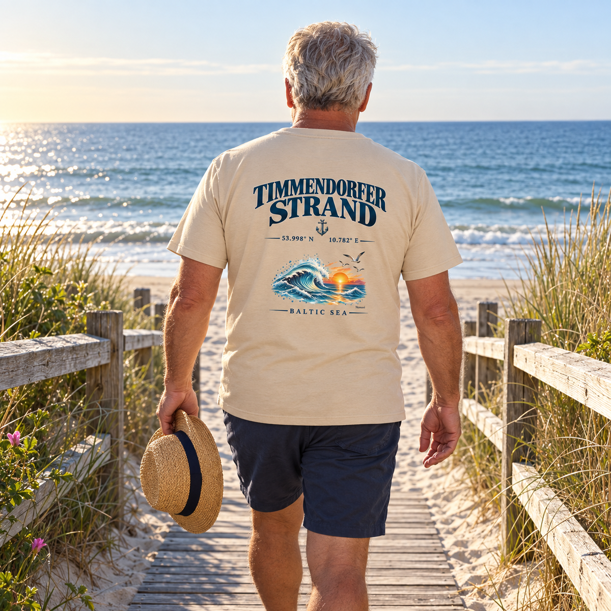 Mann im Natural-farbenen Essential-T-Shirt mit Timmendorfer Strand – Baltic Sea Rückenprint am Strandzugang.